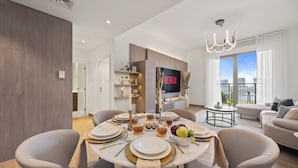 A modern living room with a dining area, a flat-screen TV, and a balcony with a view.