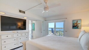 Un dormitorio con una cama grande, un televisor de pantalla plana, un ventilador de techo y vista al océano a través de una puerta corrediza.