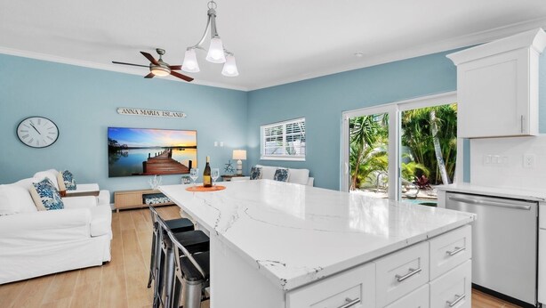 A modern kitchen with a white island, a ceiling fan, and a view of a tropical garden through a glass door.