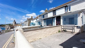 A coastal street with a stone wall, a bench, and a building with a sign reading "Coastline Cafe." - Perfectly located to enjoy breathtaking sea views of Porthleven beach  & harbour (Porthleven)