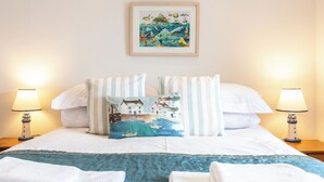 A neatly made bed with white bedding, striped pillows, and a coastal-themed throw blanket. - Perfectly located to enjoy breathtaking sea views of Porthleven beach  & harbour (Porthleven)