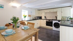 A modern kitchen with white cabinets, a built-in washing machine, and a dining area with a wooden table set for two. - Perfectly located to enjoy breathtaking sea views of Porthleven beach  & harbour (Porthleven)