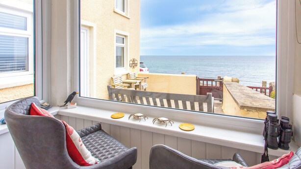 A room with a view of the sea, a window sill with binoculars, and a chair with a cushion. - Perfectly located to enjoy breathtaking sea views of Porthleven beach  & harbour (Porthleven)