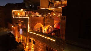 A historic stone bridge with arches, illuminated by warm lighting, connecting two buildings. - Ali Paşa Konağı (Mardin)