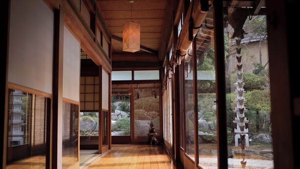 Um interior japonês tradicional com portas deslizantes, soalho de madeira e vista para um jardim com uma pagoda.
