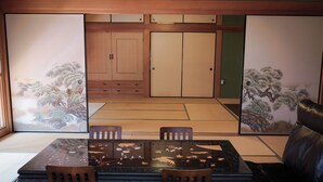 Um quarto japonês tradicional com tatames, uma mesa baixa com cadeiras e portas deslizantes com obras de arte.