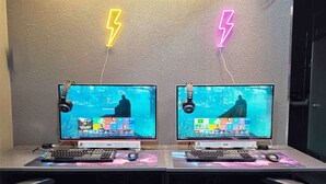 Two computer workstations with monitors, keyboards, and mice, against a textured wall with neon lightning decorations. - Anyang 3S Fashion Hotel (Anyang)