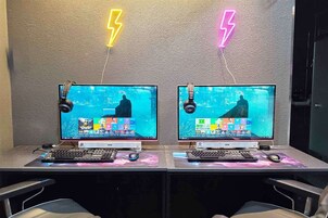 Duas estações de trabalho com monitores, teclados e ratos, em frente a uma parede texturizada com detalhes de raios em neon.