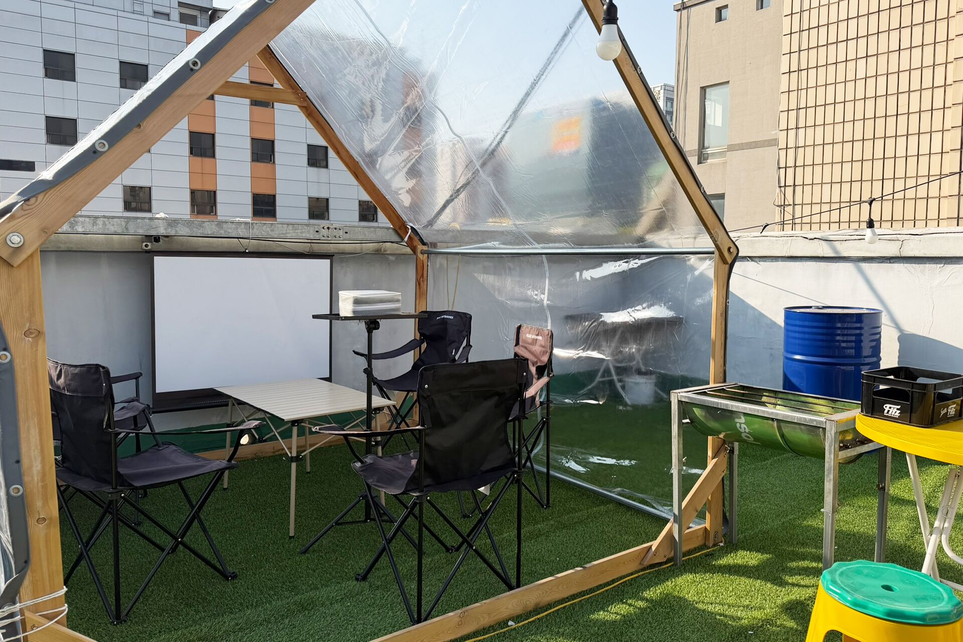 A greenhouse structure with a transparent roof, artificial grass, and various items like a table, chairs, and containers.
