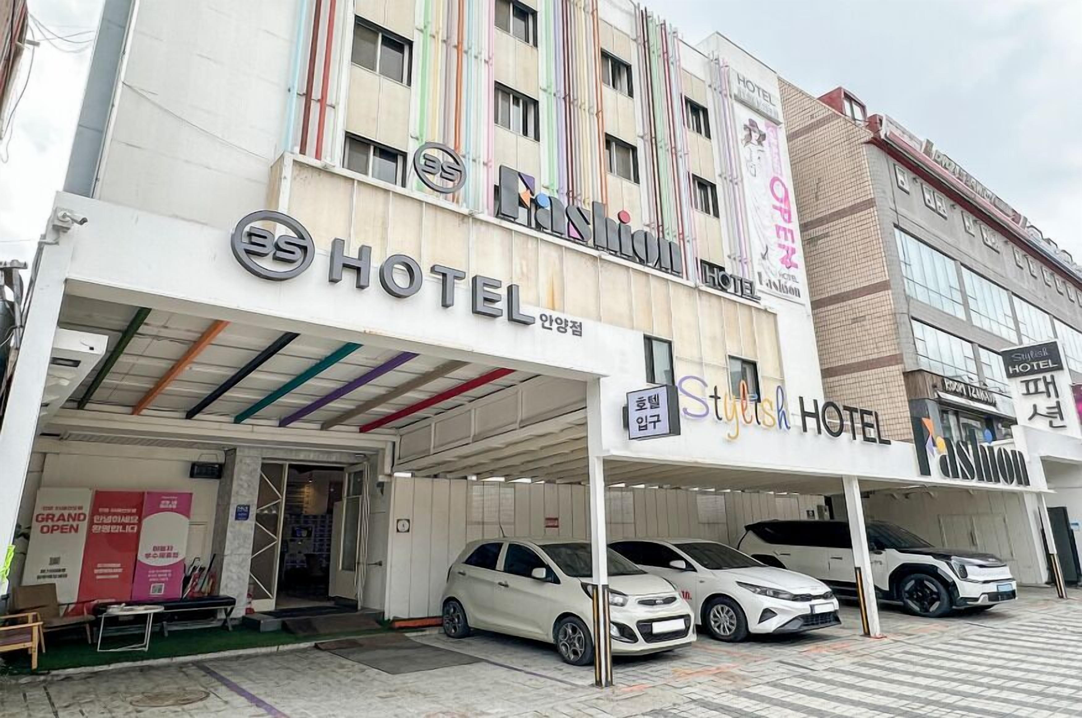 A hotel with a modern facade, multiple floors, and a covered parking area with several cars parked.