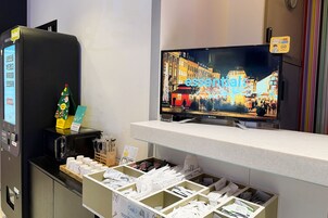 Uma área de recepção de hotel com uma tela digital exibindo uma vista urbana, uma máquina de venda automática e um pequeno pinheiro de Natal.