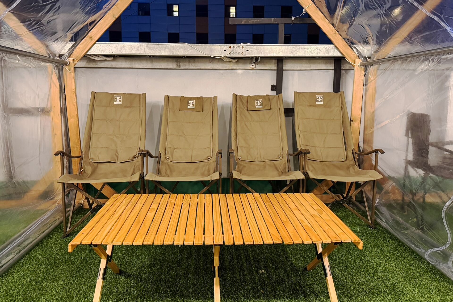 A tent with four chairs and a wooden table, surrounded by transparent walls.
