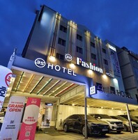 Um hotel com fachada moderna, sinalização iluminada e uma área de estacionamento coberta com vários carros.