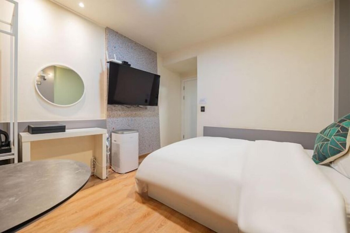 Una habitación de hotel moderna con una cama, un escritorio, un televisor de pantalla plana y un pequeño purificador de aire.