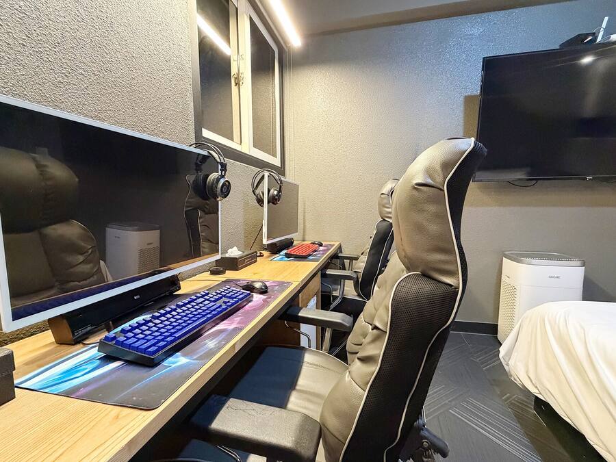 Habitación de hotel con escritorio, computadora, audífonos, cama y televisor.
