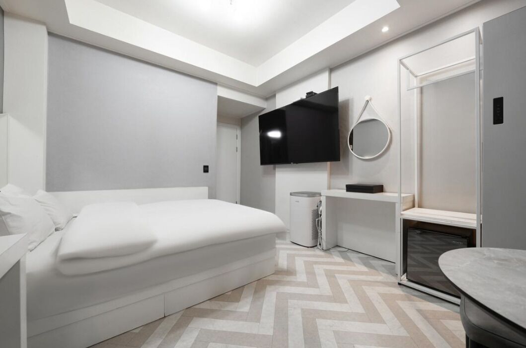 Een moderne slaapkamer met een bed, een televisie, een spiegel en een klein tafeltje.