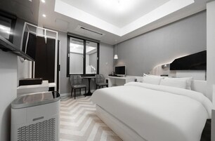 Quarto de hotel moderno com uma cama grande, uma escrivaninha, uma cadeira, uma televisão e uma luminária no teto.