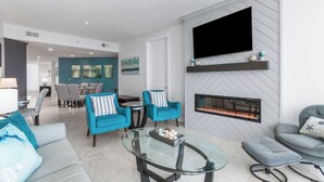 Ein modernes Wohnzimmer mit Kamin, Flachbildfernseher und Essbereich im Hintergrund.