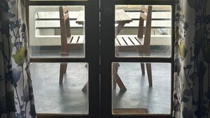 A room with a large window offering a view of palm trees and buildings. There are two wooden chairs and a table in front of the window. - Jess Beach Villa (Galle)