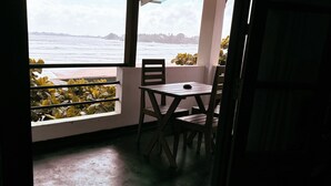 A balcony with a table and chairs, overlooking a body of water and distant land. - Jess Beach Villa (Galle)