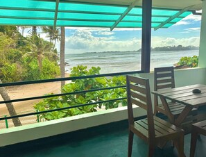 A balcony with a view of the ocean, a wooden table, and chairs.