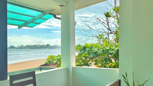 A room with a wooden table and chairs, a potted plant, and a view of the beach and ocean through large windows. - Jess Beach Villa (Galle)