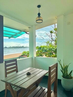 A room with a wooden table and chairs, a potted plant, and a view of the beach and ocean through large windows. - Jess Beach Villa (Galle)