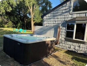 A hot tub outside a house with a wooden deck and a window.