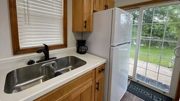 A kitchen with wooden cabinets, a stainless steel sink, a white refrigerator, and a window with blinds. - Waterfront legacy farm cottage house with WiFi, AC in lovely Eau Claire (Eau Claire)