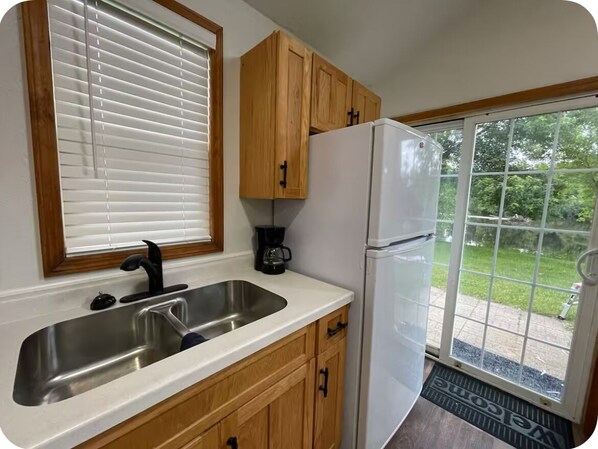 A kitchen with wooden cabinets, a stainless steel sink, a white refrigerator, and a window with blinds.