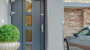 Entrada de un edificio moderno con una puerta gris, una planta en maceta y un automóvil estacionado.