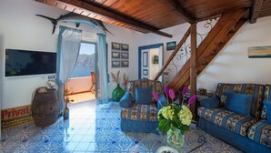 A cozy living room with a wooden ceiling, a large fish mounted on the wall, a patterned sofa, and a TV on the wall. - Domus Ursula timeless charm (Praiano)
