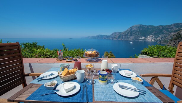 A table set for breakfast with a scenic view of the sea and mountains. - Domus Ursula timeless charm (Praiano)