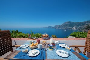 A table set for breakfast with a scenic view of the sea and mountains.