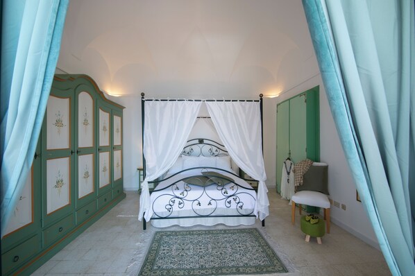A bedroom with a four-poster bed, a green wardrobe, a chair, and a small stool.