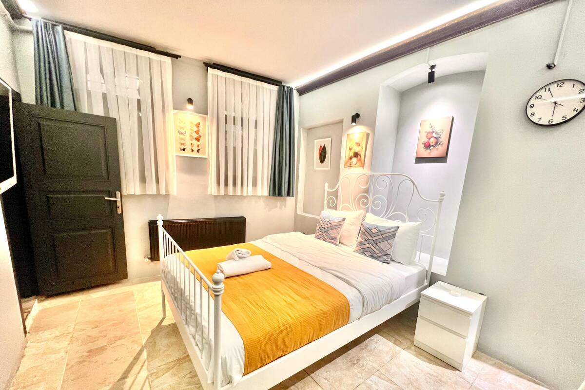 A modern bedroom with a bed, bedside tables, a clock, and curtains.