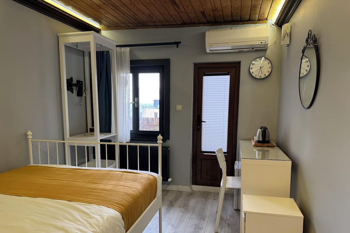 A bedroom with a bed, a chair, a desk, an air conditioner, a window, and a door.