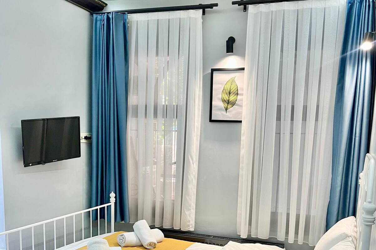A neatly made bed with a yellow and white bedspread, white pillows, and a bedside table with two black bowls.