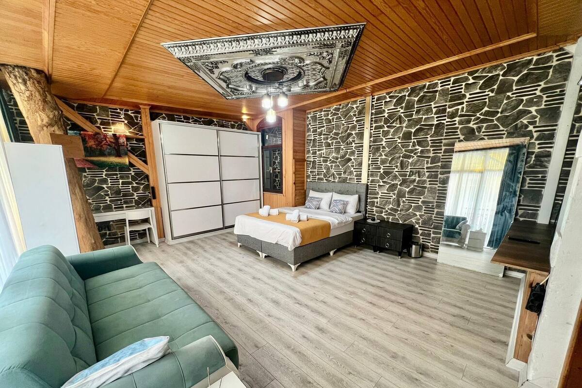 A modern bedroom with a bed, a green sofa, a stone wall, and a wooden ceiling.