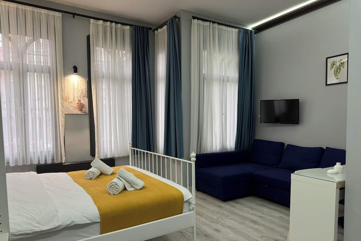 A modern hotel room with a bed, a sofa, a TV, and a small cabinet.