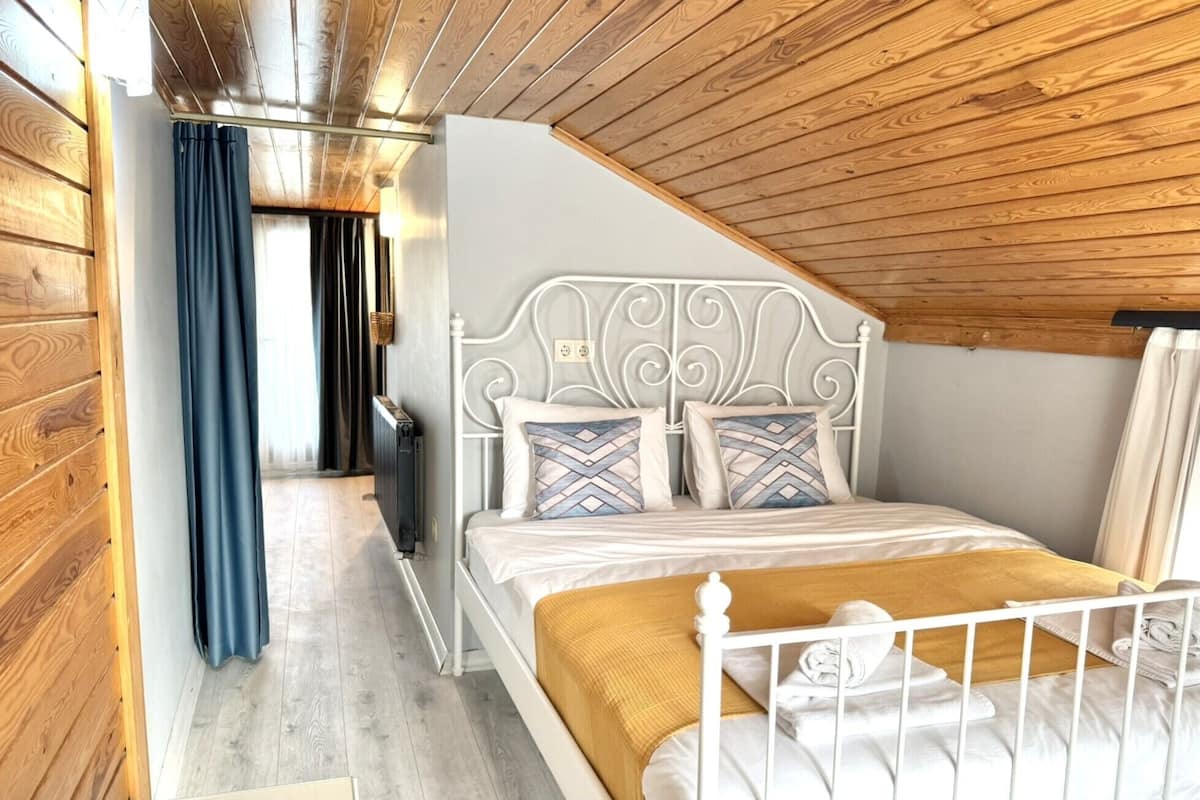 A bedroom with a sloped ceiling, wooden walls, a white metal bed frame, and a wooden floor.