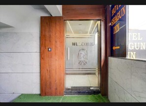 A hotel entrance with a wooden door, a welcome sign, and a directional arrow to the right. - hotel shagun inn bopal (Ahmedabad)