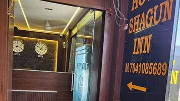A hotel reception area with a wooden reception desk, a clock, and a sign for Hotel Shagun Inn.