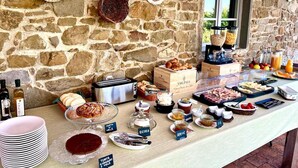 A breakfast buffet with various food items and condiments, set against a stone wall backdrop. - La Locanda Volpaia (Radda in Chianti)