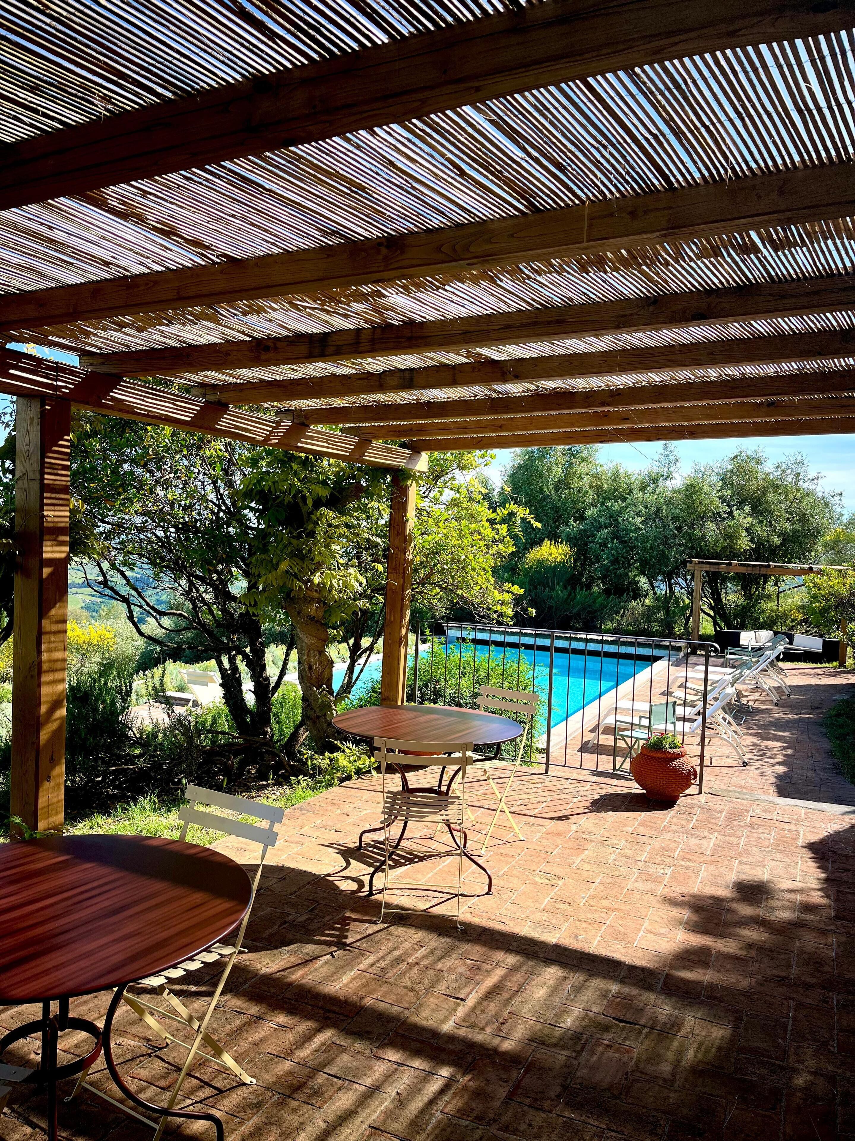 Un espacio al aire libre techado con piscina, pérgola de madera y asientos.