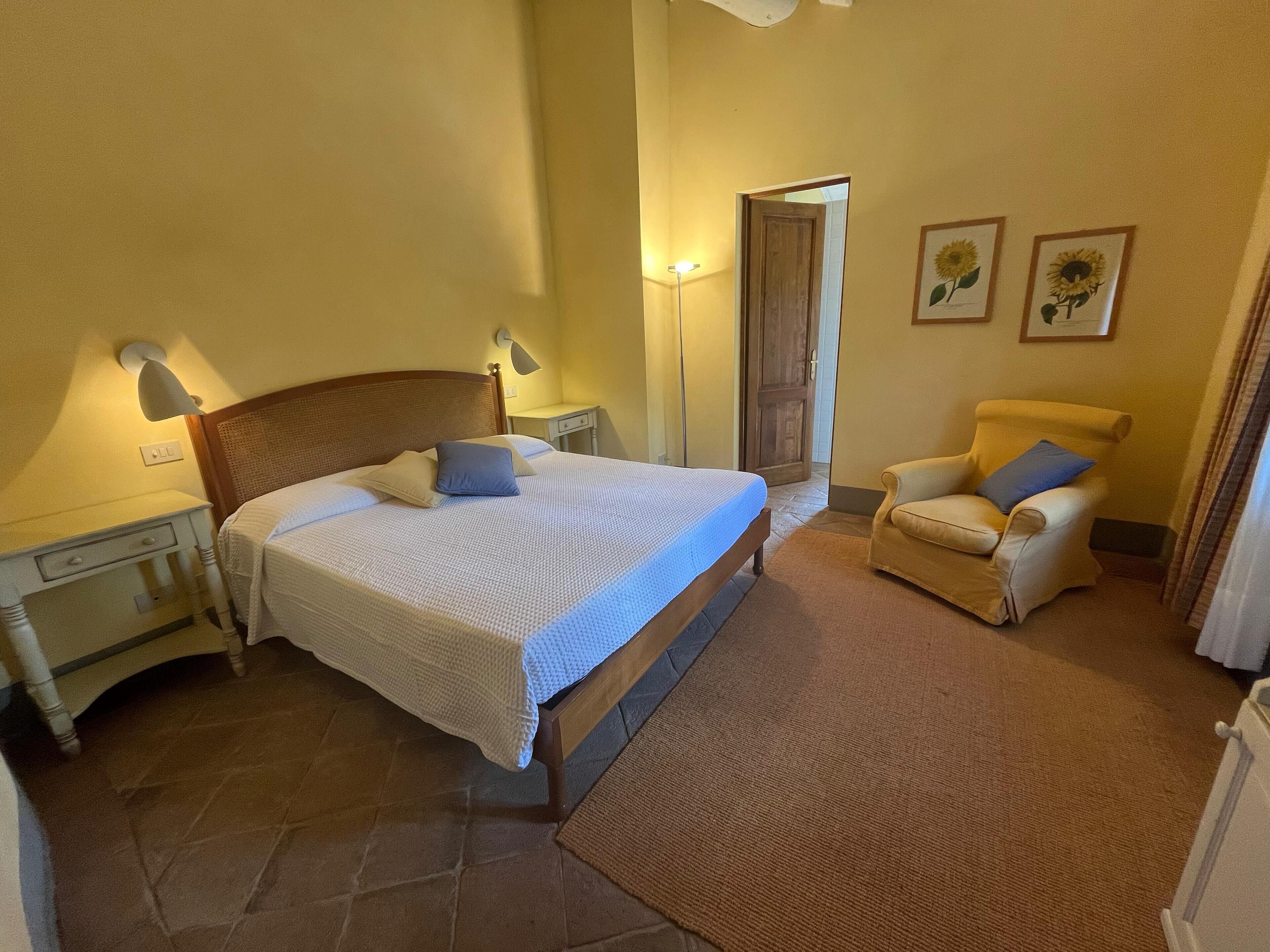 Une chambre à coucher avec un lit, des tables de chevet, une chaise, une lampe et une porte.