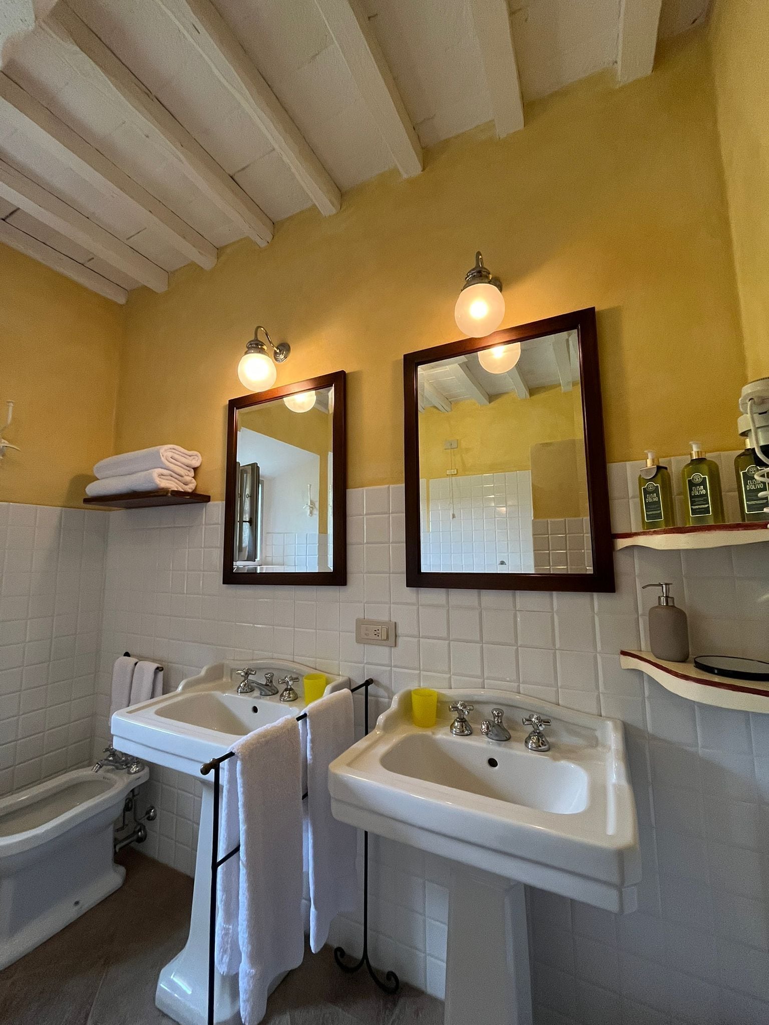 A bathroom with two sinks, a bathtub, and two mirrors. There are towels on a shelf and toiletries on a counter.