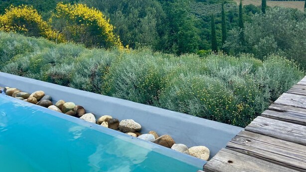 A wooden deck with a swimming pool, surrounded by lush greenery and a mountainous landscape. - La Locanda Volpaia (Radda in Chianti)
