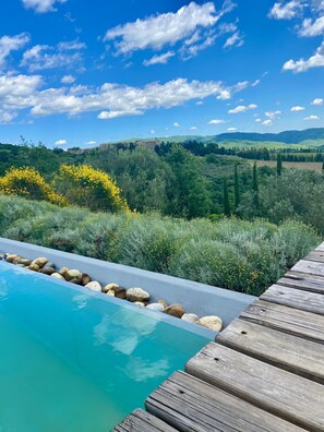 A wooden deck with a swimming pool, surrounded by lush greenery and a mountainous landscape. - La Locanda Volpaia (Radda in Chianti)