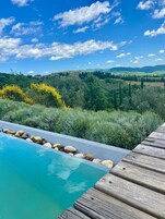 Una terraza de madera con piscina, rodeada de exuberante vegetación y un paisaje montañoso.